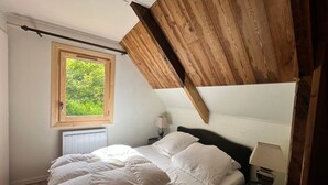 Ein Schlafzimmer mit schrägemausertem Dach, einem Fenster mit Blick auf Grünflächen, einem Bett mit weißer Bettwäsche und einem Nachttisch mit Lampe.