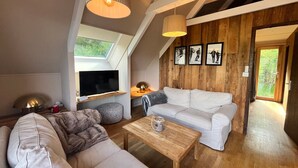 Ein modernes Wohnzimmer im Loft-Stil mit hohen Decken, Holzbalken, einem weißen Sofa, einem Couchtisch aus Holz und einem an einer Holzablage montierten Fernseher.