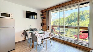 Comedor con mesa preparada para cuatro personas, refrigerador, microondas y un ventanal con vistas a un bosque.