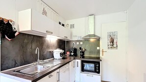 Una cocina compacta con armarios blancos, horno empotrado, cocina y lavamanos.