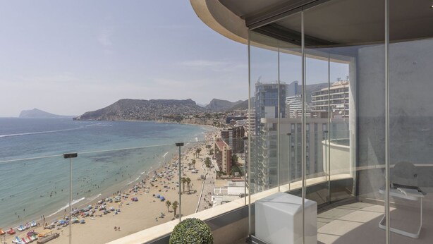 Un balcon offrant une vue sur une plage, un paysage urbain et une montagne au loin.