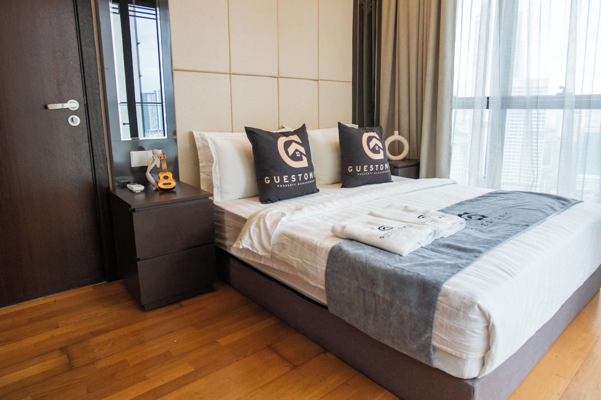 A modern hotel room with a large bed, a nightstand with a ukulele, and a view of the city through the window.