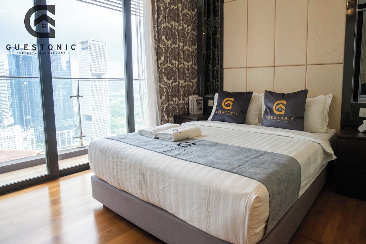 A modern hotel room with a large bed, a city view, and branded pillows.