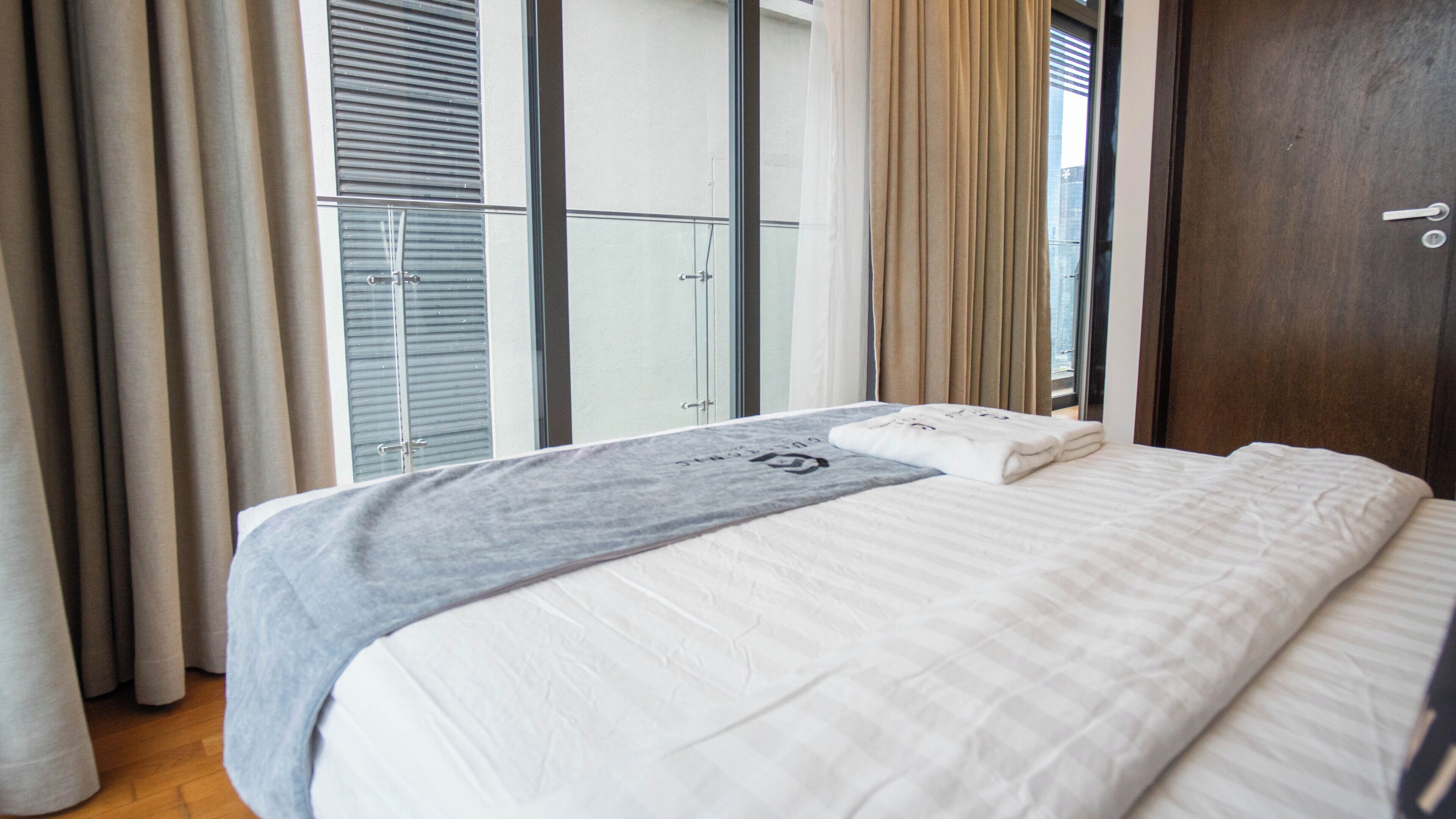 A hotel room with a large bed, a window with blinds, and a view of a balcony.