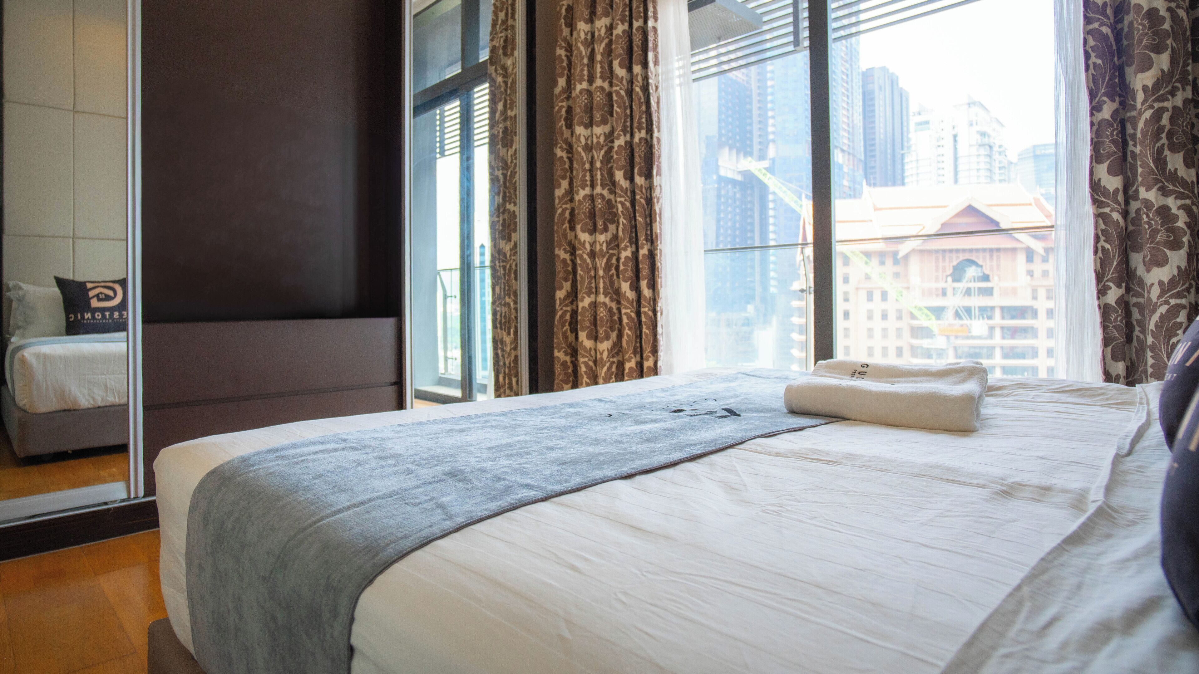 A hotel room with a large bed, a view of the cityscape, and a window with curtains.