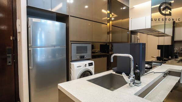 A modern kitchen with stainless steel appliances, a built-in oven, microwave, and a washing machine. - Dorsett Residence KL by Guestonic (Kuala Lumpur)