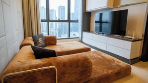 Habitación de hotel moderna con dos sofás marrones tapizados, un televisor de pantalla plana grande y vista a la ciudad a través del ventanal.
