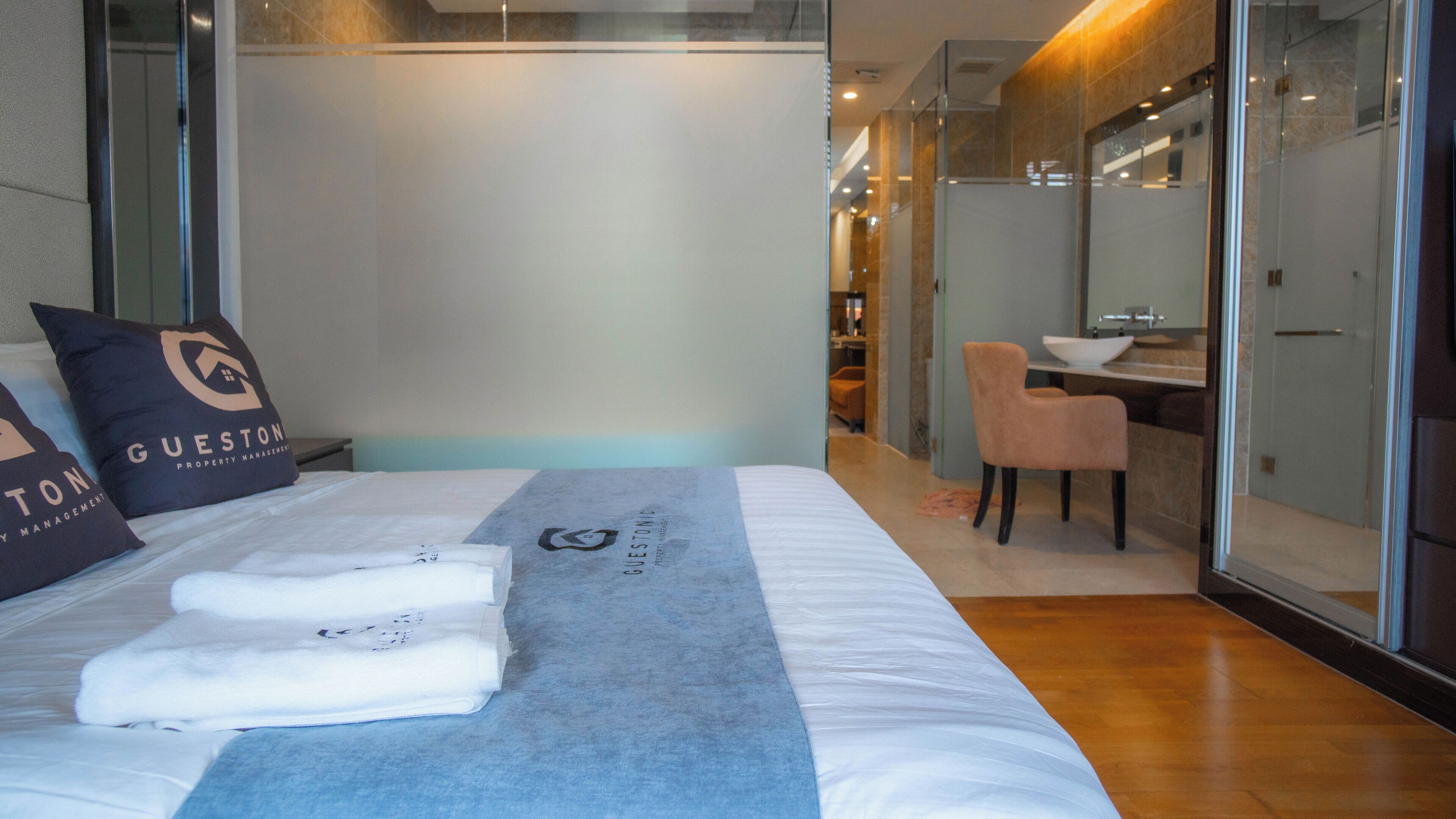 Una habitación de hotel moderna con una cama, un separador de vidrio, un escritorio pequeño y una silla.