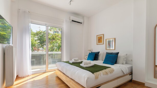 A modern bedroom with a wooden bed, white bedding, and a green throw. - Artsi - 3BR Apt w Balcony in Athens (Athens)