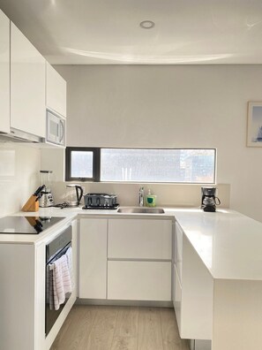 A modern kitchen with white cabinetry, a built-in oven, a microwave, a coffee maker, and a window providing natural light. - Edificio Area 93  (Bogotá)