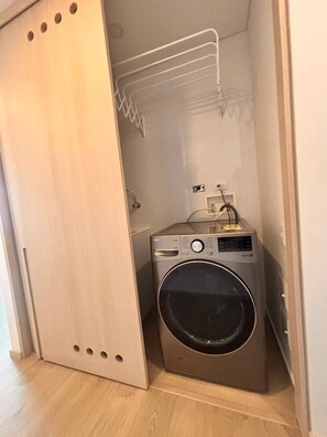 A compact laundry room with a washing machine, a drying rack, and a small shelf. - Edificio Area 93  (Bogotá)