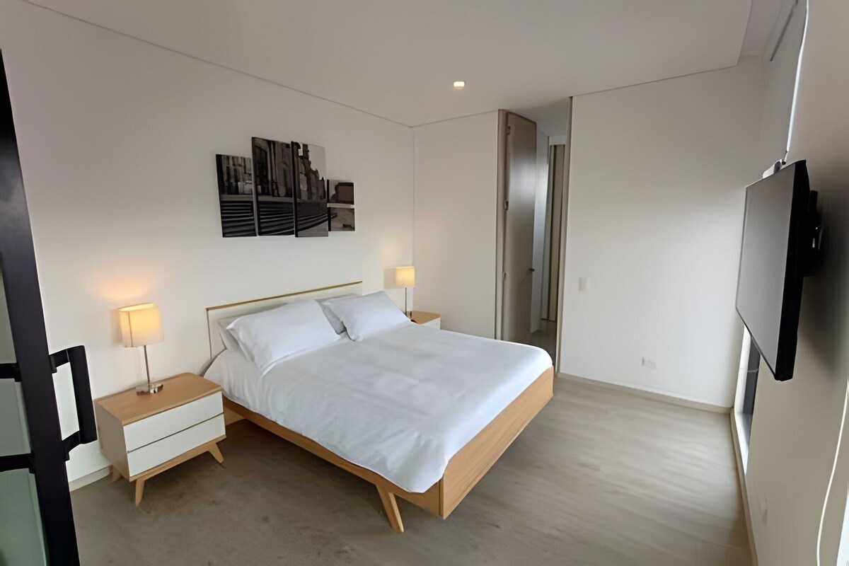 A modern bedroom with a bed, bedside tables, a wall-mounted TV, and a door.