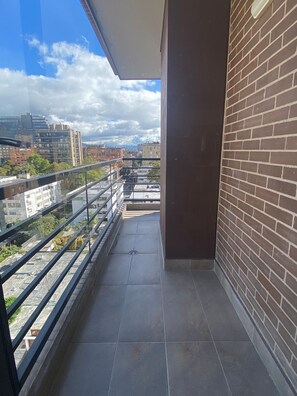 A balcony with a view of a cityscape, a brick wall, and a tiled floor. - Edificio Area 93  (Bogotá)