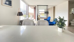 A modern living room with a large table, two chairs, a potted plant, and a view of the city through large windows. - Edificio Area 93  (Bogotá)