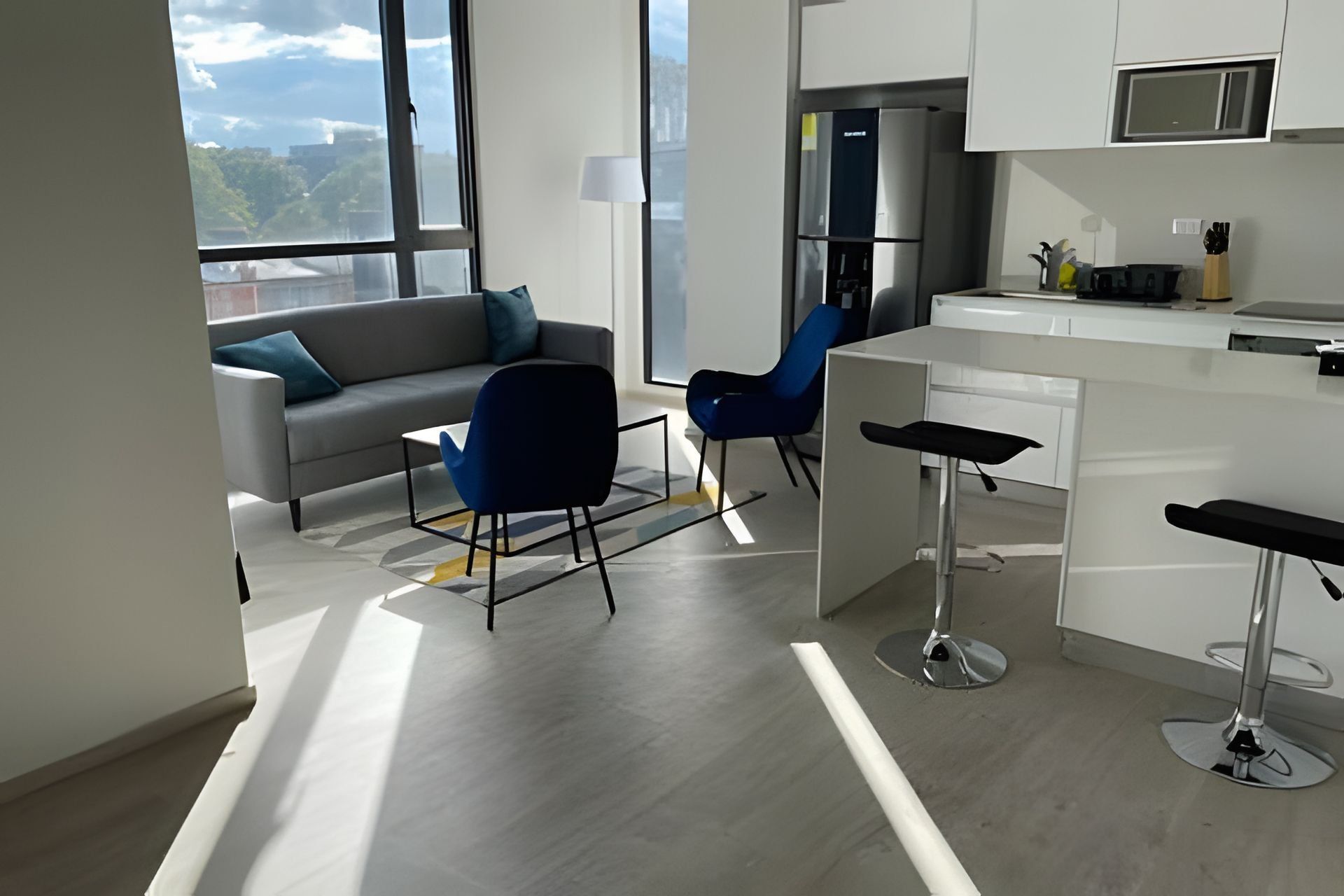 A modern kitchen with white cabinets, a stainless steel refrigerator, and a bar area with stools.