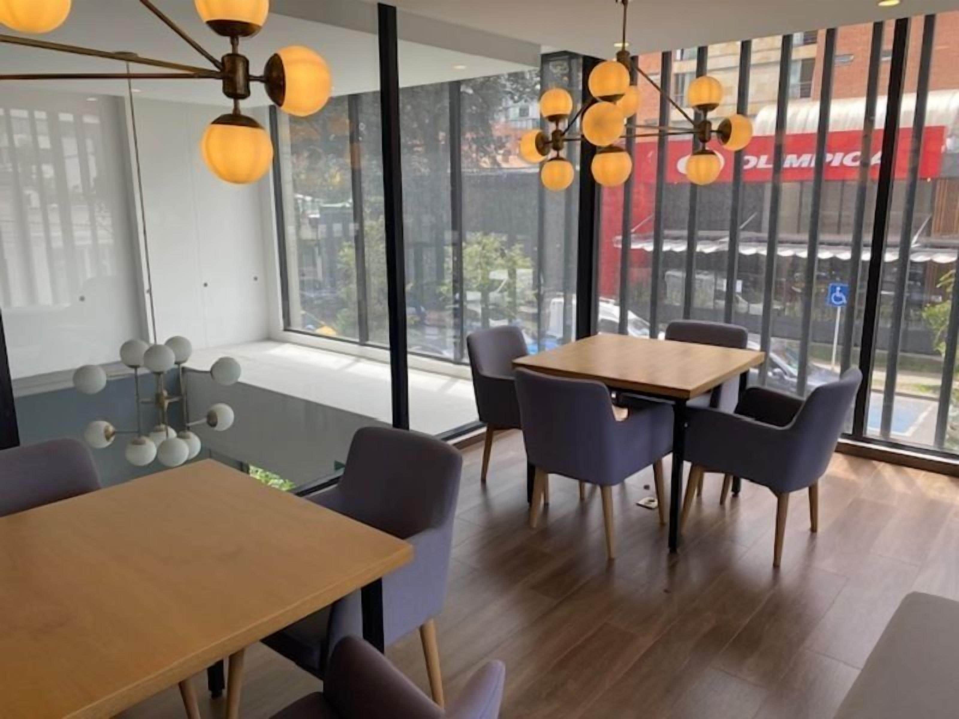 Un espace de restauration moderne avec une table et des chaises en bois, de grandes fenêtres et un lustre sphérique original.