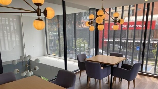 A modern dining area with a wooden table and chairs, large windows, and a unique spherical chandelier. - Edificio Area 93  (Bogotá)