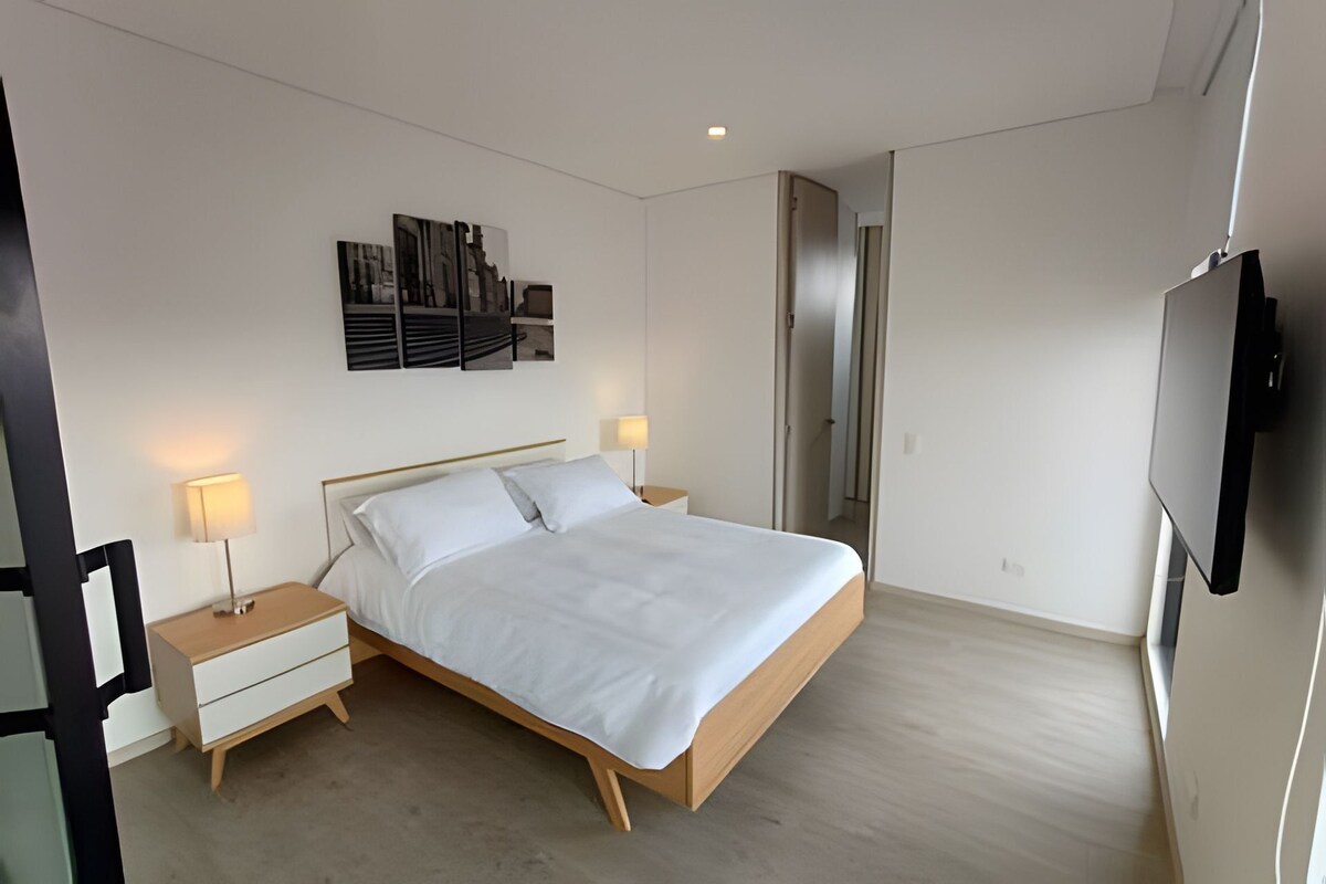 A modern bedroom with a bed, bedside tables, a wall-mounted TV, and a door.
