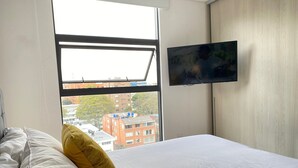 A hotel room with a bed, a window, and a TV mounted on the wall. - Edificio Area 93  (Bogotá)