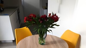 A dining area with a round wooden table, two yellow chairs, and a vase with red flowers. - Edificio Area 93  (Bogotá)
