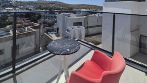 Eine Dachterrasse mit Glasgeländer, einem roten Sessel, einem kleinen runden Tisch und freiem Blick auf die Stadtlandschaft.
