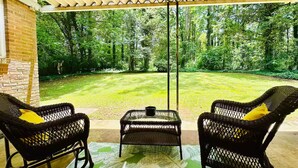 A covered patio with wicker chairs and a table, overlooking a well-maintained lawn and trees. - Cozy home near Latta Nature Preserve (Huntersville)