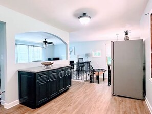 A modern kitchen with dark cabinetry, a wooden countertop, and a central island. There is a dining area with a table and chairs, and a staircase leading to another level.