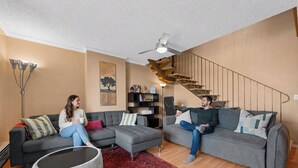 A modern living room with two grey sofas, a red patterned rug, and a staircase with wooden railings.