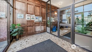 A hotel entrance with a wooden panel wall, a glass door, and a doormat.