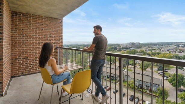 A balcony with a brick wall, two yellow chairs, and a table.