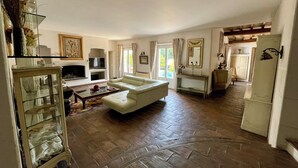 A spacious living room with a white sofa, a television, and a fireplace. - BASTIDE DE L'ORANGERAIE SWIMMING POOL AIR CONDITIONING (Vence)