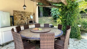 An outdoor patio with a round table, wicker chairs, a brick fireplace, and a hanging lantern. - BASTIDE DE L'ORANGERAIE SWIMMING POOL AIR CONDITIONING (Vence)