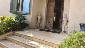 A stone staircase leading to a wooden door with a decorative panel, a hanging light fixture, and a window with blue shutters. - BASTIDE DE L'ORANGERAIE SWIMMING POOL AIR CONDITIONING (Vence)