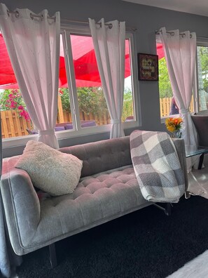 Un canapé gris agrémenté d’un coussin moelleux et d’un plaid à carreaux, une table basse en verre et un vase rempli de fleurs.