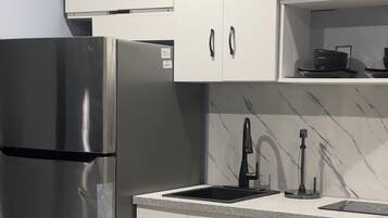 Una cocina moderna con armarios blancos, un refrigerador de acero inoxidable, un grifo negro y un salpicadero de mármol.