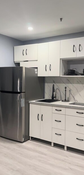 A modern kitchen with white cabinets, a stainless steel refrigerator, a black faucet, and a marble backsplash.