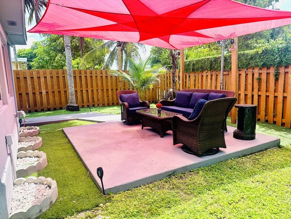 Une terrasse avec des meubles d’extérieur, un parasol rouge et une clôture en bois.