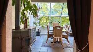 Een knus vertrek met een open haard, rieten stoelen en uitzicht door grote ramen.
