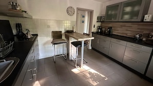 Een moderne keuken met een houten tafel, twee barkrukken, een klok aan de muur en roestvrijstalen apparatuur.