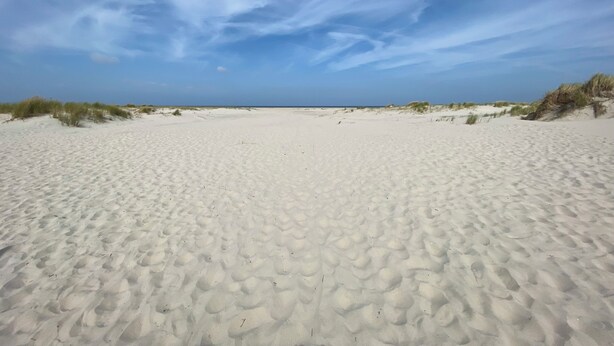 Een breed zandstrand met duinen aan weerszijden en een heldere lucht.