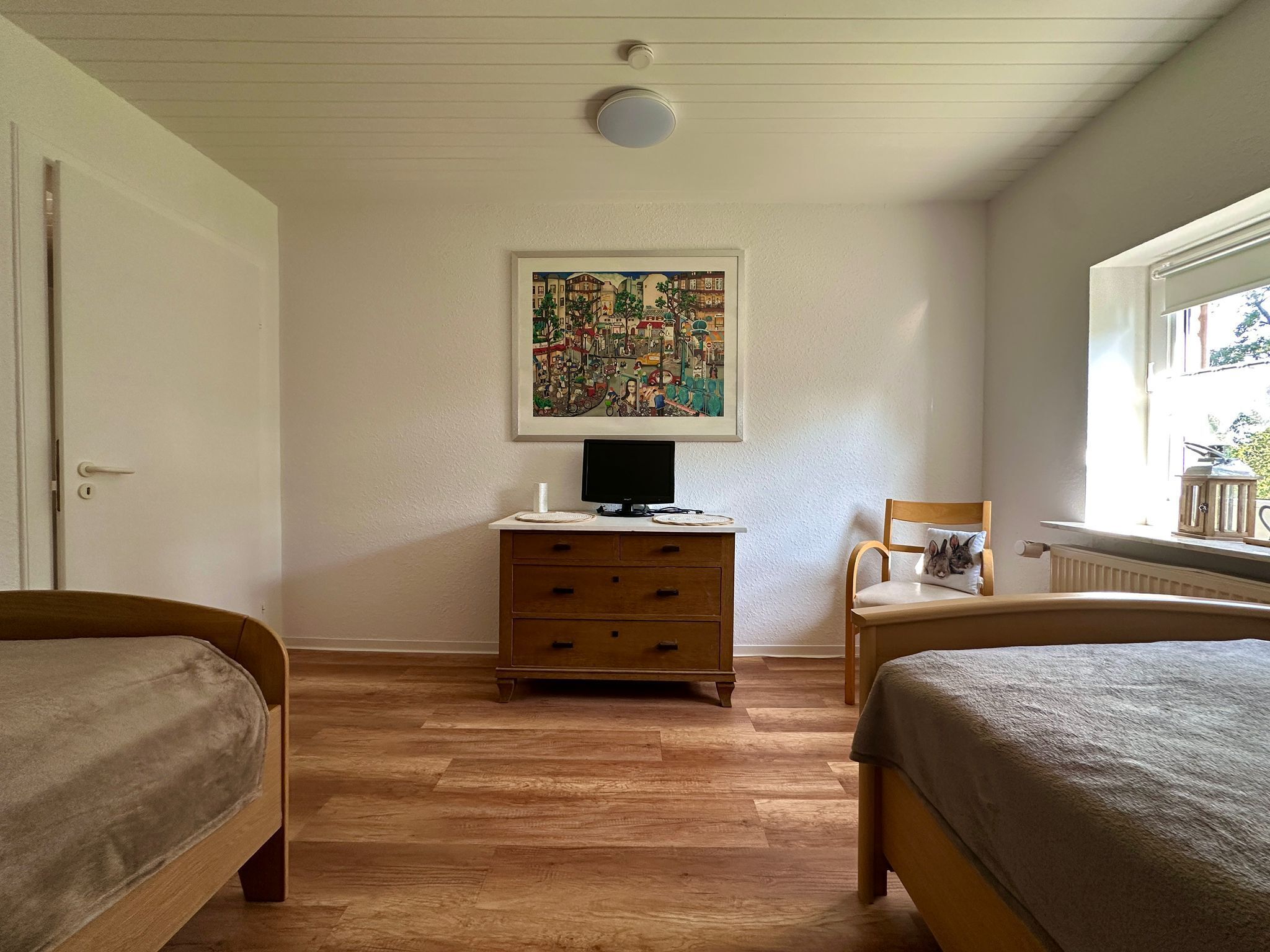 Une chambre à coucher avec deux lits en bois, une commode en bois, un tableau encadré accroché au mur et une fenêtre donnant sur un paysage verdoyant.