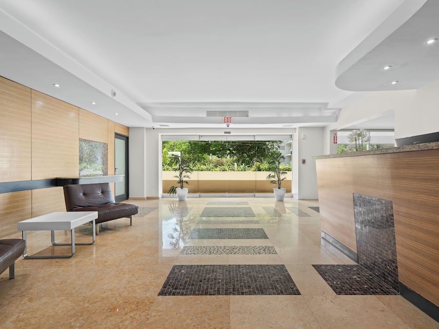 A modern lobby with a reception desk, seating area, and a view of greenery outside.