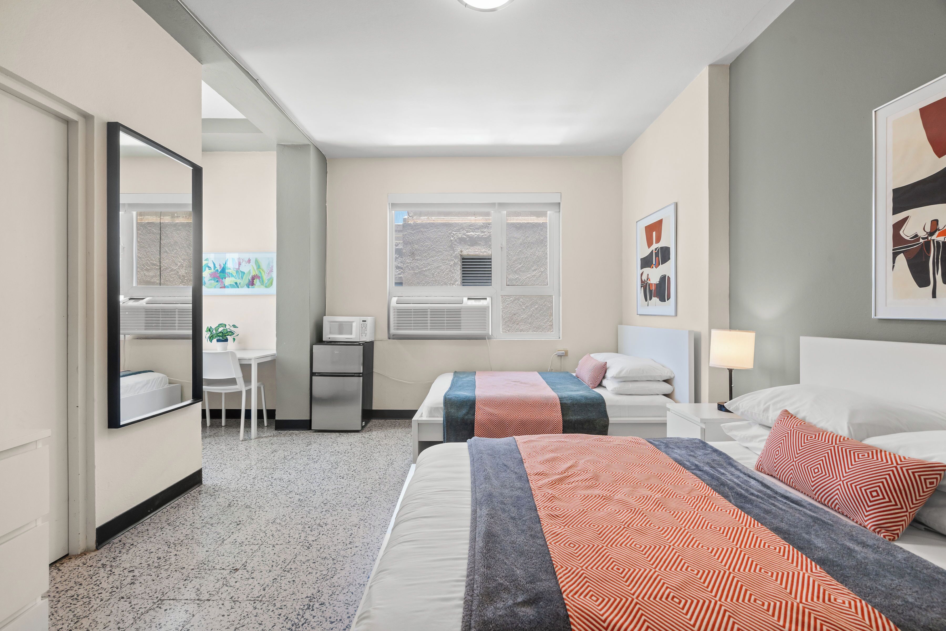 Ein Hotelzimmer mit zwei Betten, einem Schreibtisch, einem Stuhl und einem Fenster mit Jalousien.