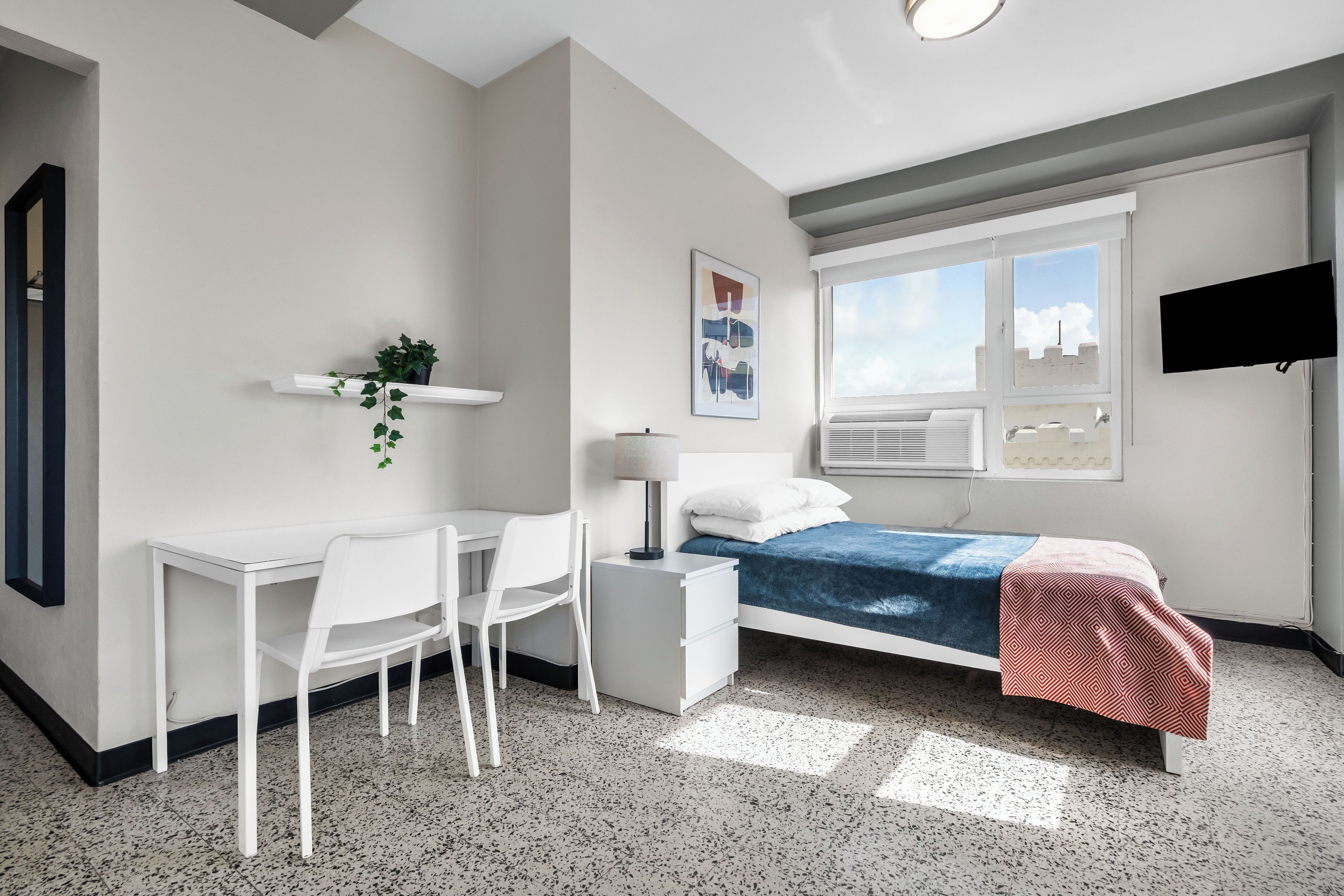 A modern bedroom with a bed, desk, chair, and a TV.