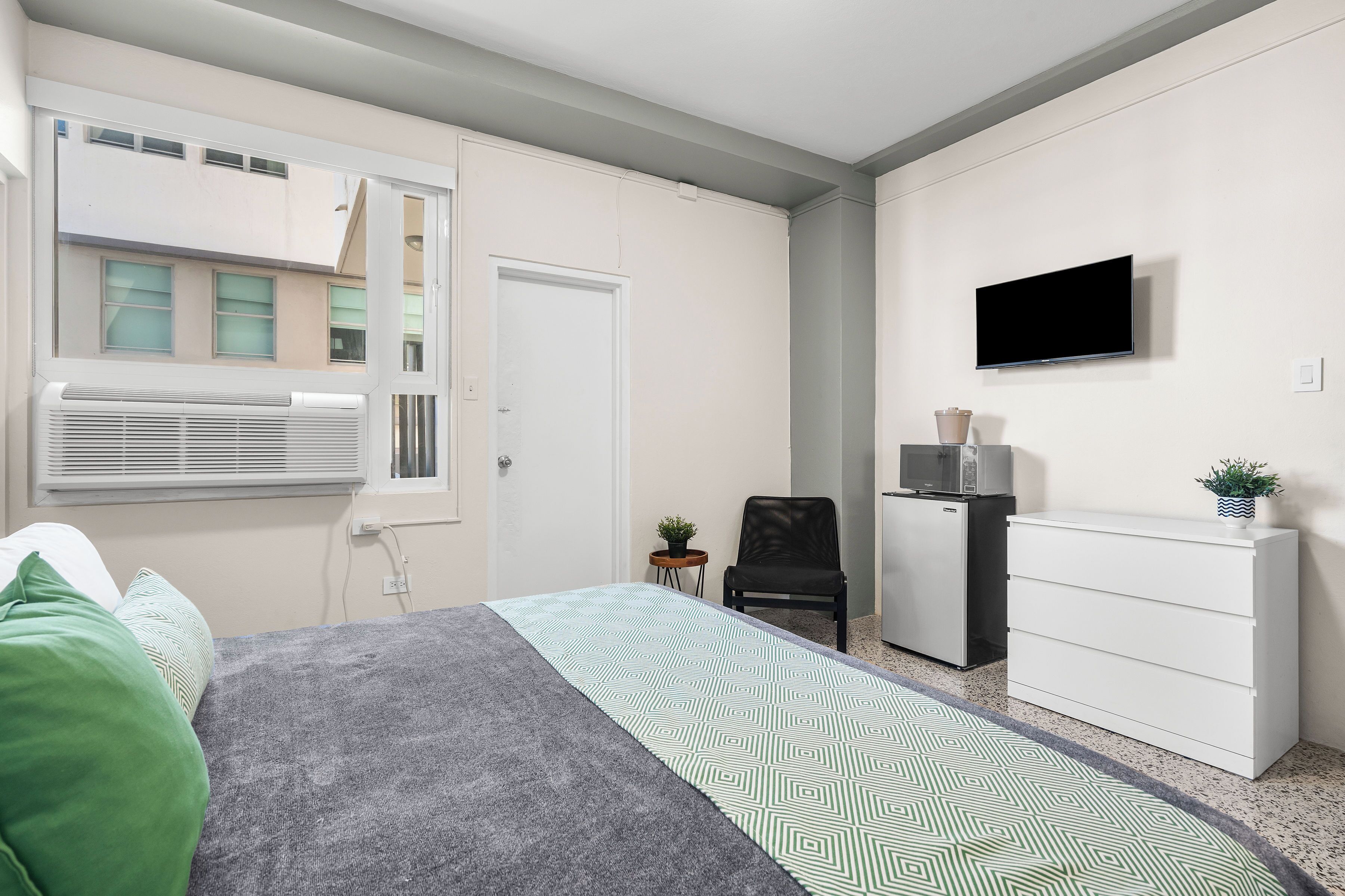 Un dormitorio con cama, escritorio, silla, televisor y ventana.