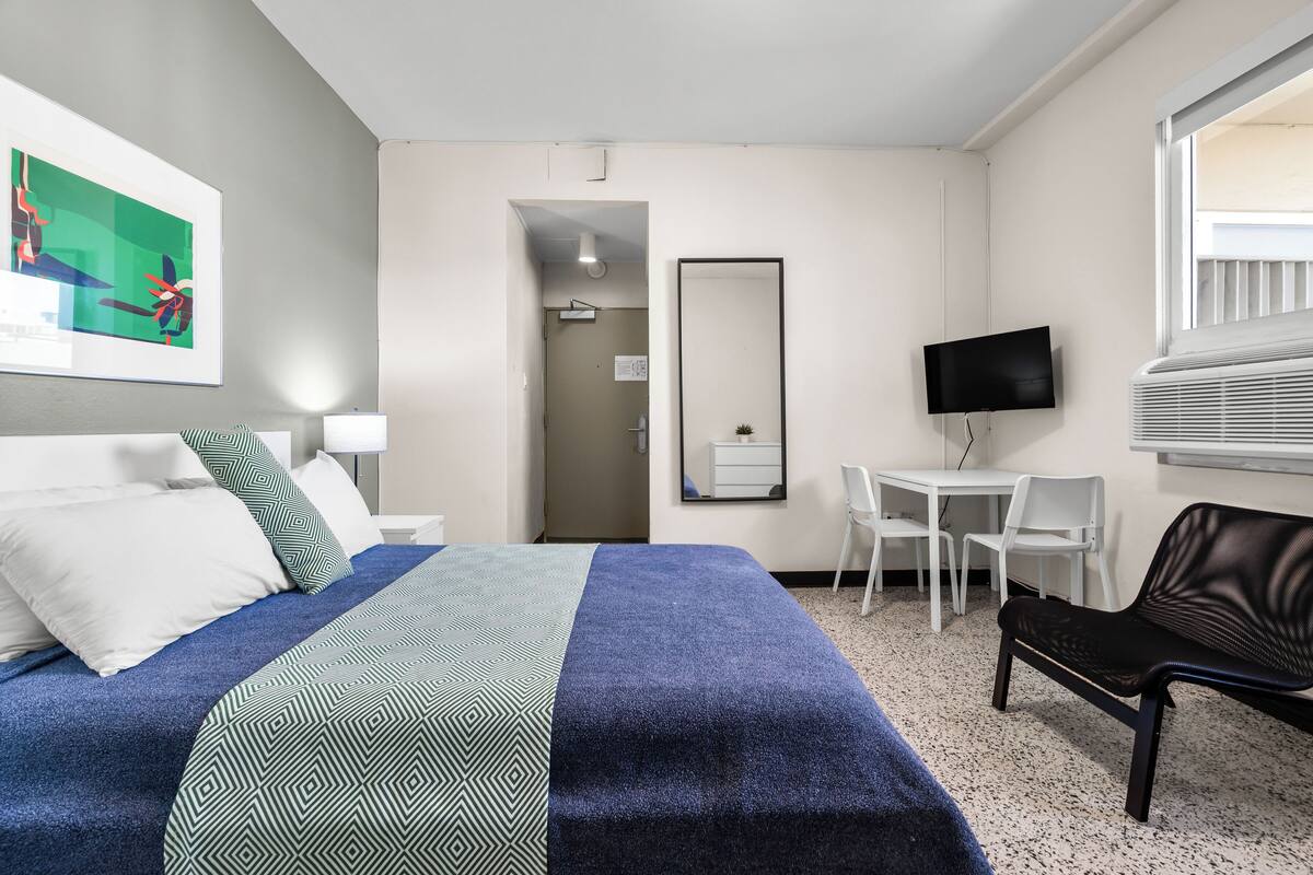 A hotel room with a bed, a desk, a chair, a TV, and a window.