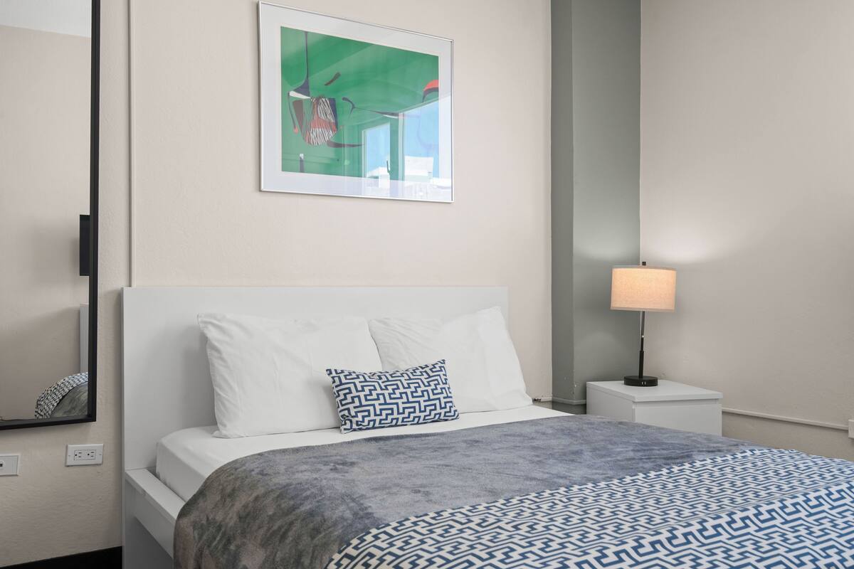 A neatly made bed with a patterned blanket, a bedside lamp, and a framed artwork on the wall.