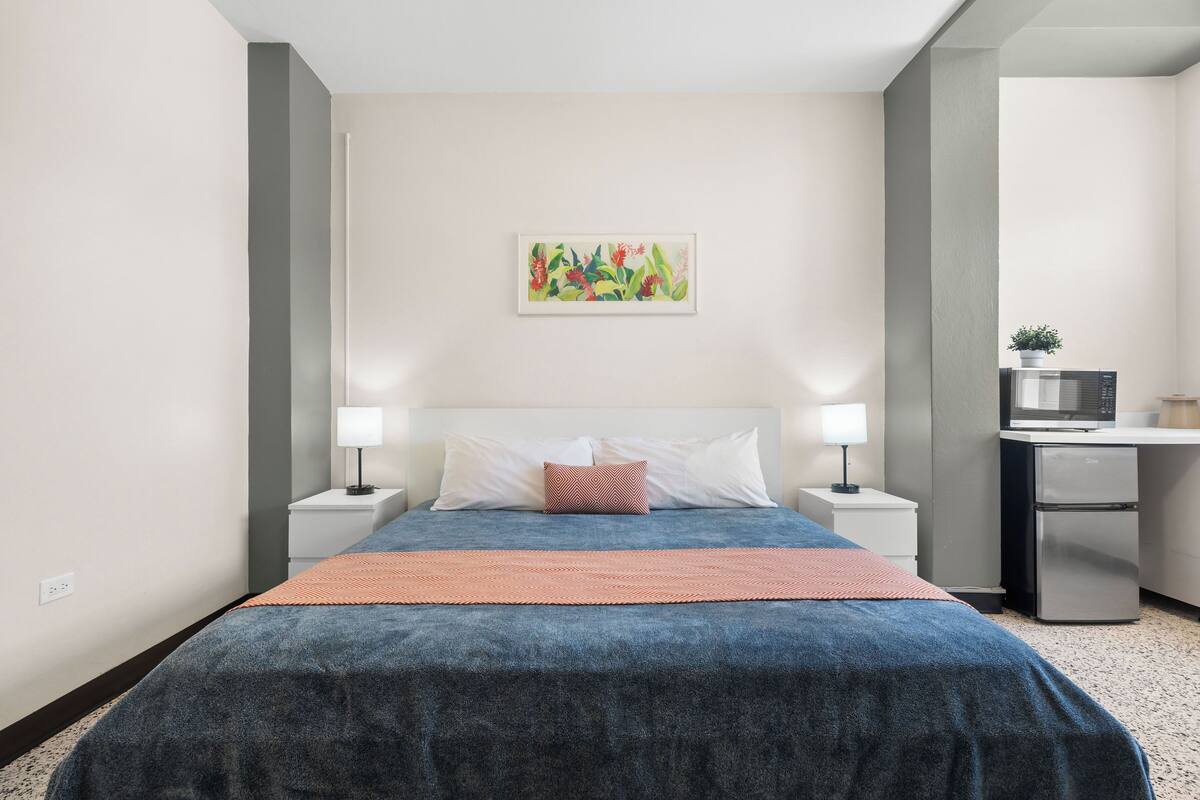 A modern hotel room with a bed, nightstands, a desk, and a microwave.
