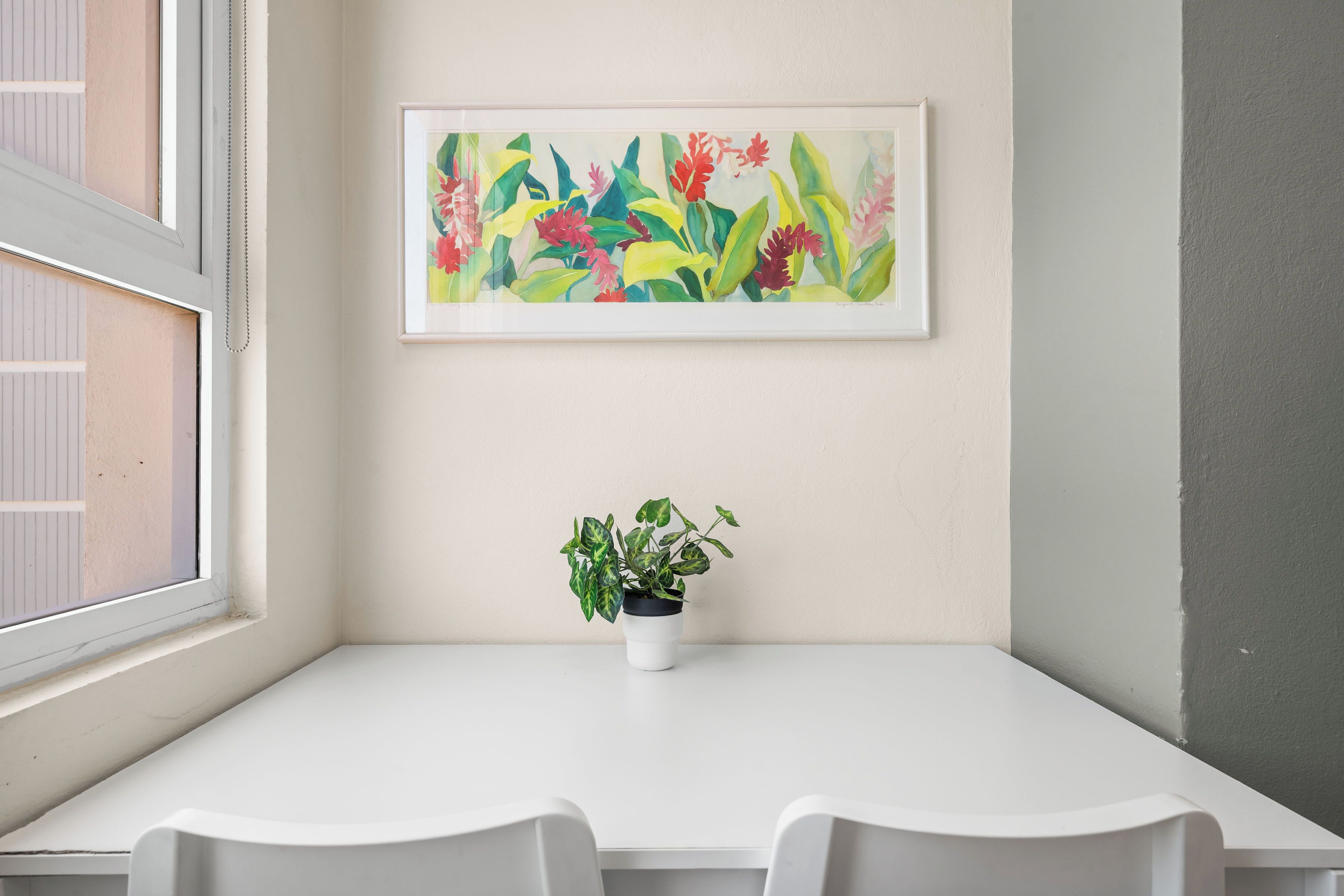 Une table blanche avec deux chaises, une plante en pot et un tableau encadré accroché au mur.