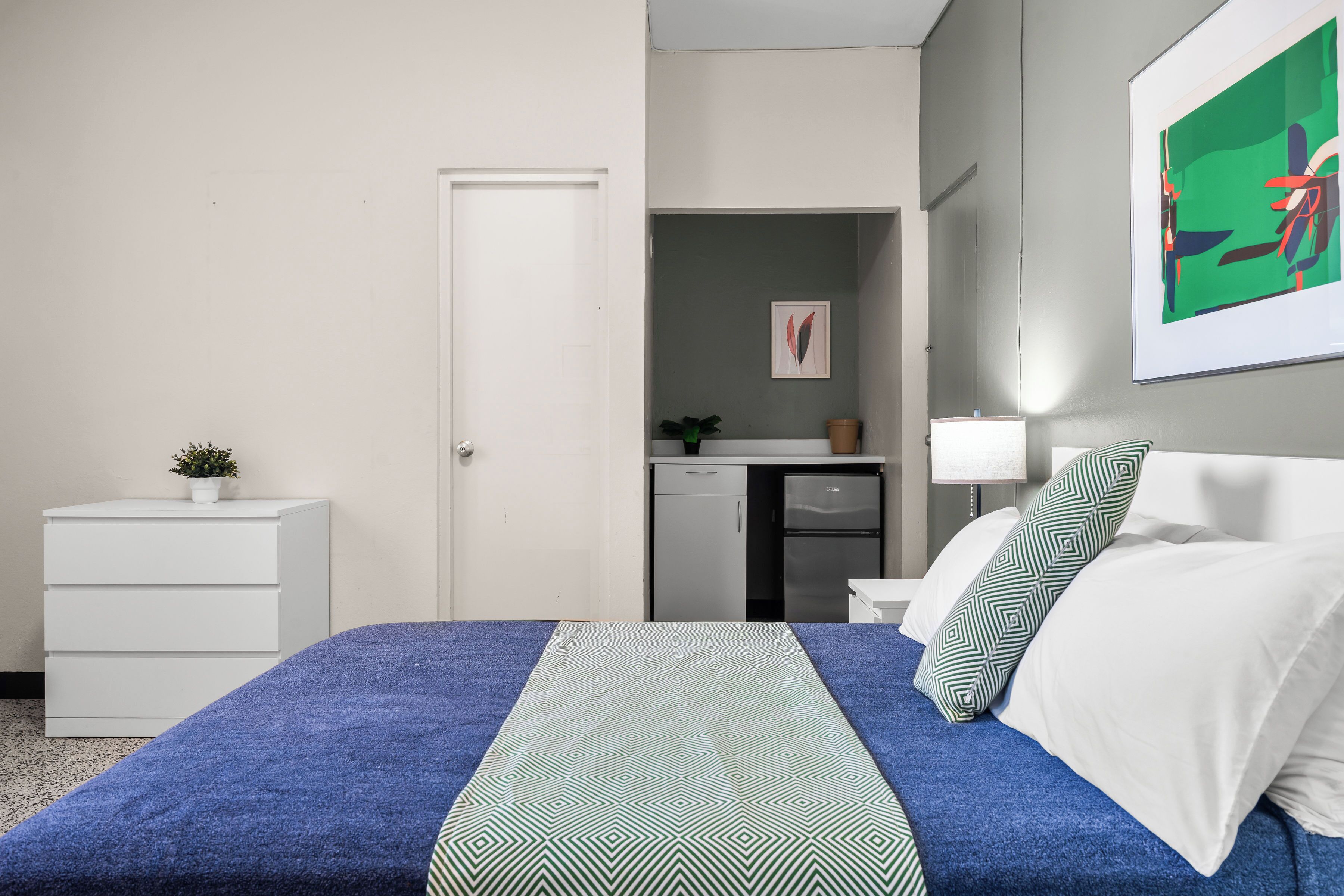 A bedroom with a bed, a dresser, a desk, and a lamp.